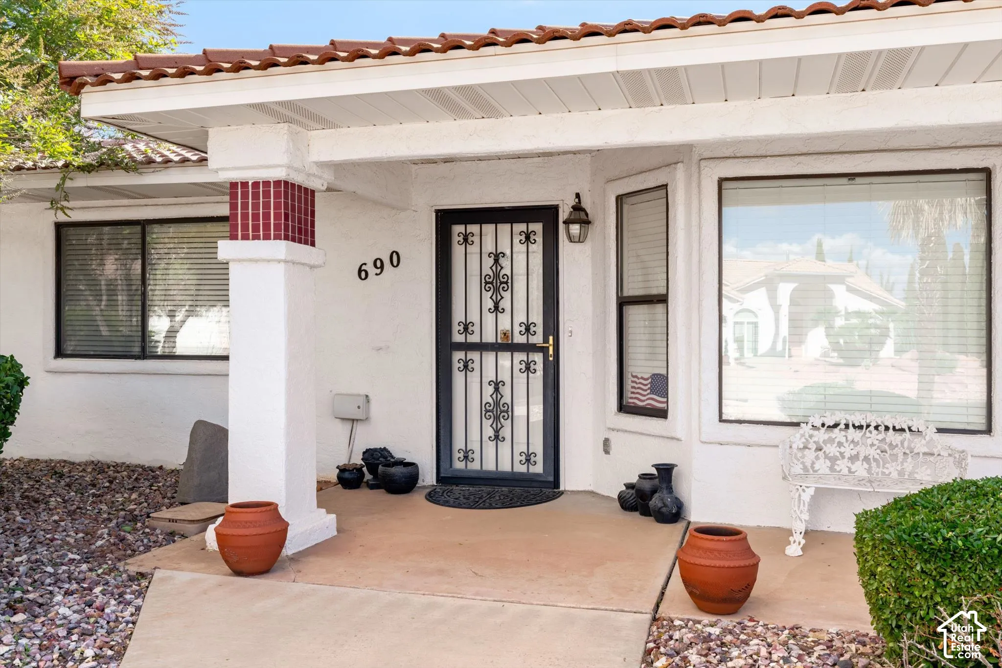 Stucco exterior featuring a covered porch, terracotta-style roof tiles, decorative column accents, and a metal security screen door
