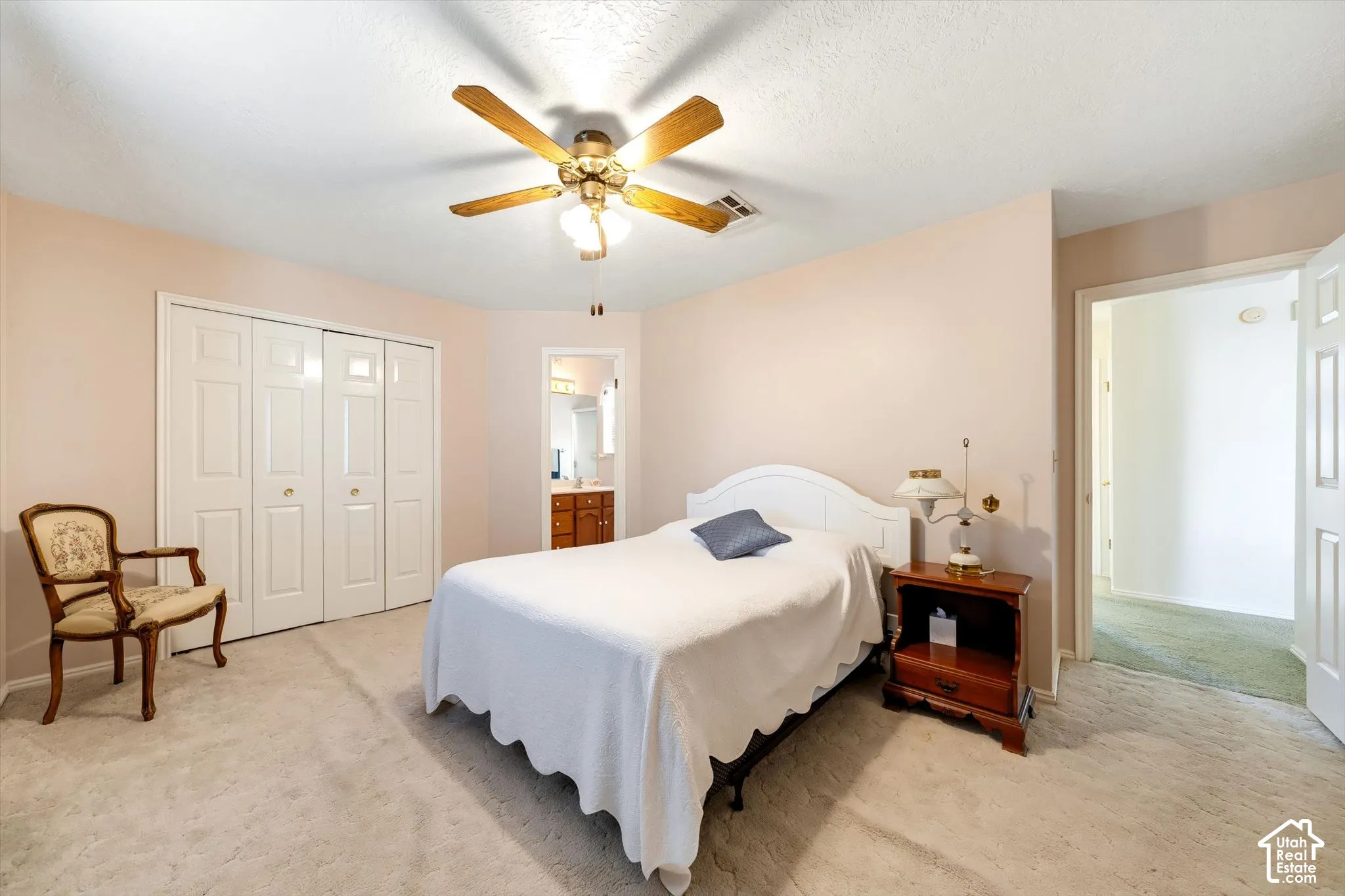 Neutral-toned interior featuring wall-to-wall carpeting, a multi-blade ceiling fan with integrated lighting, and white bi-fold closet doors