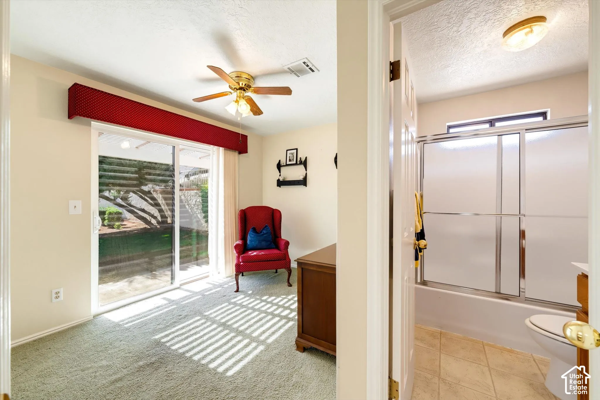 Sliding glass door with exterior patio access, carpeted flooring, ceiling fan with light fixture, and bathroom featuring a tub-shower combination with sliding glass doors