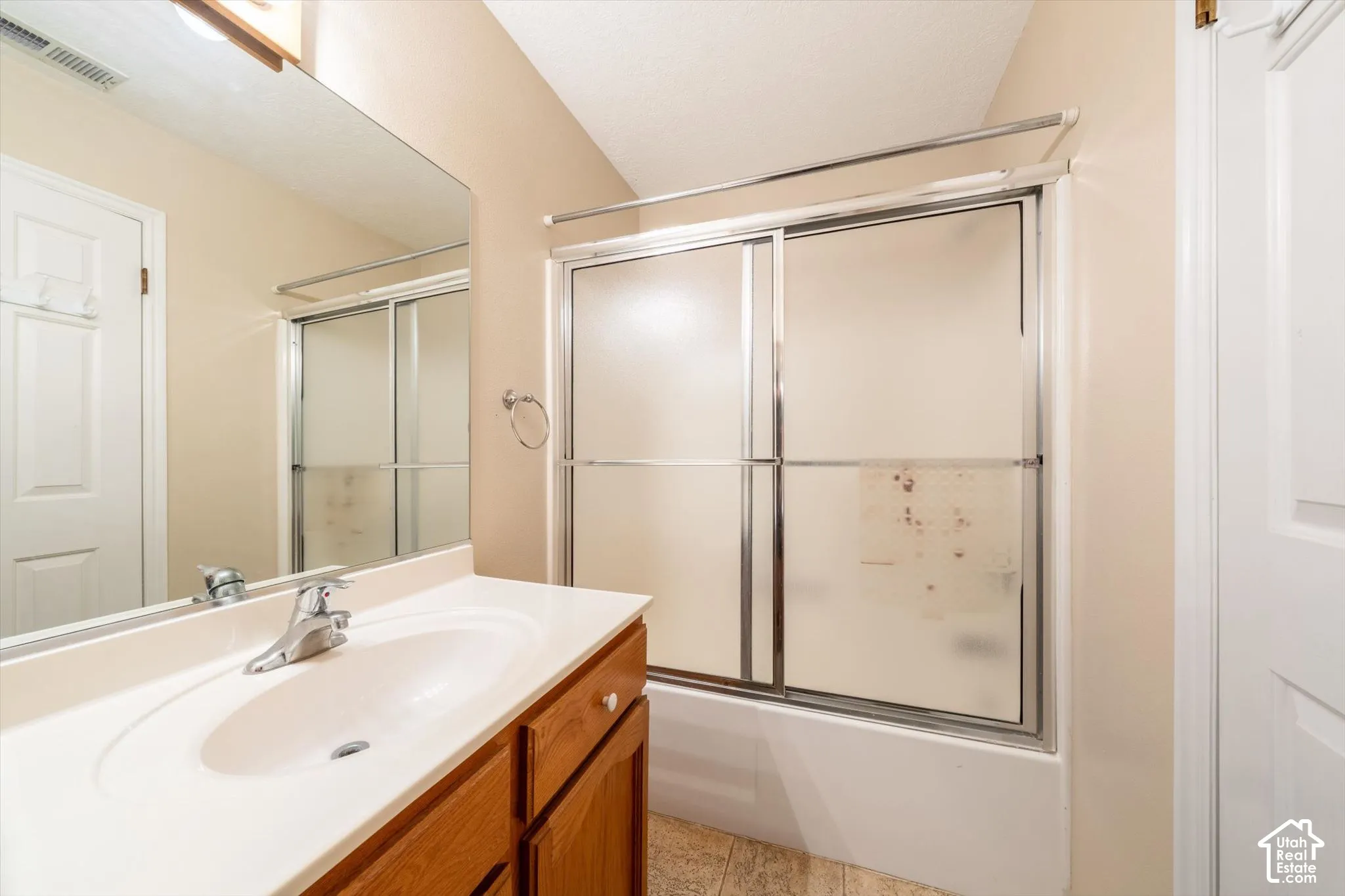 Bathroom featuring a vanity with integrated sink, chrome faucet, large vanity mirror, and a shower-tub combination with sliding glass doors