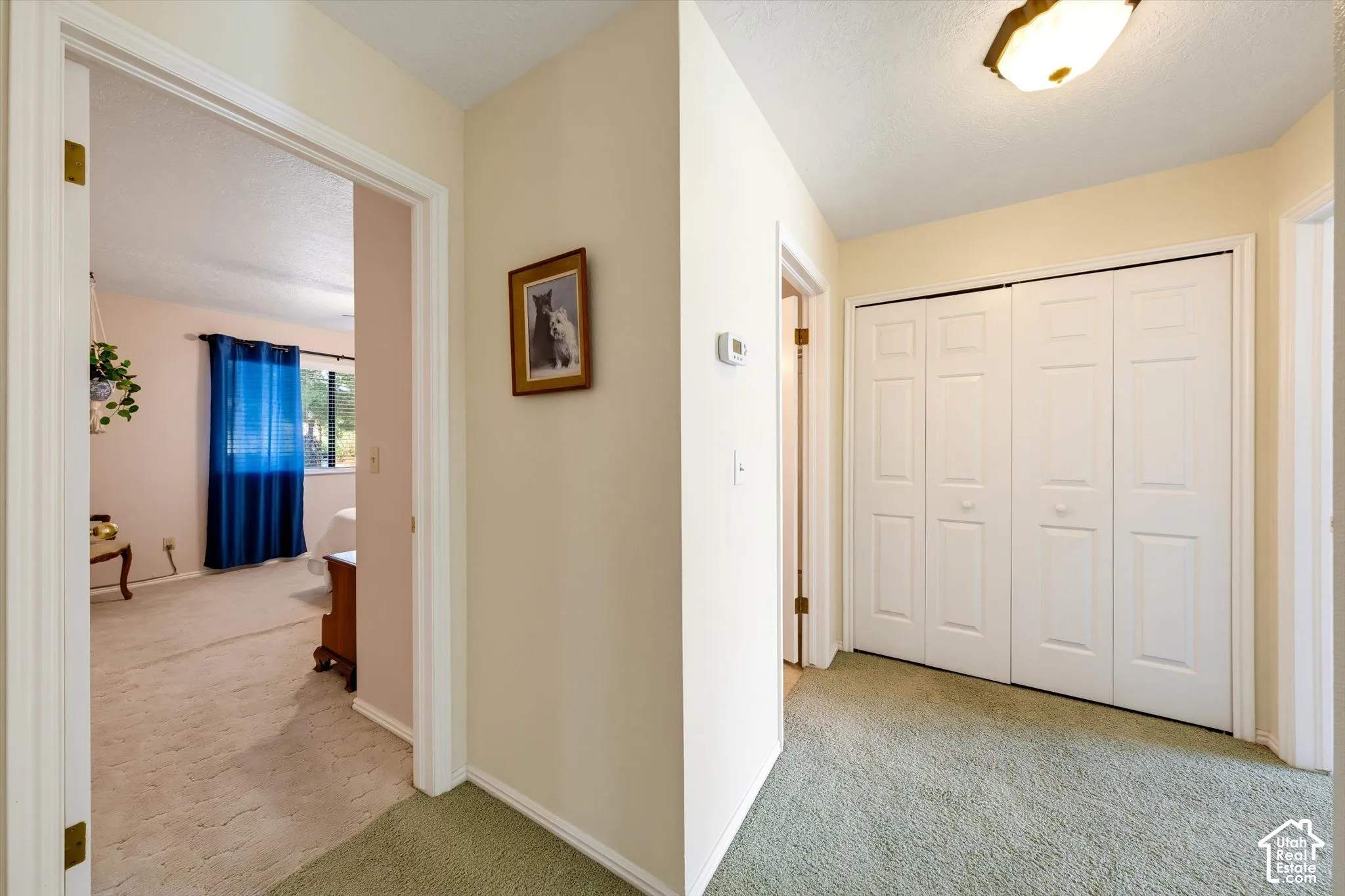 Hallway featuring dual-paneled bi-fold closet doors, wall-mounted thermostat, and overhead flush-mount lighting