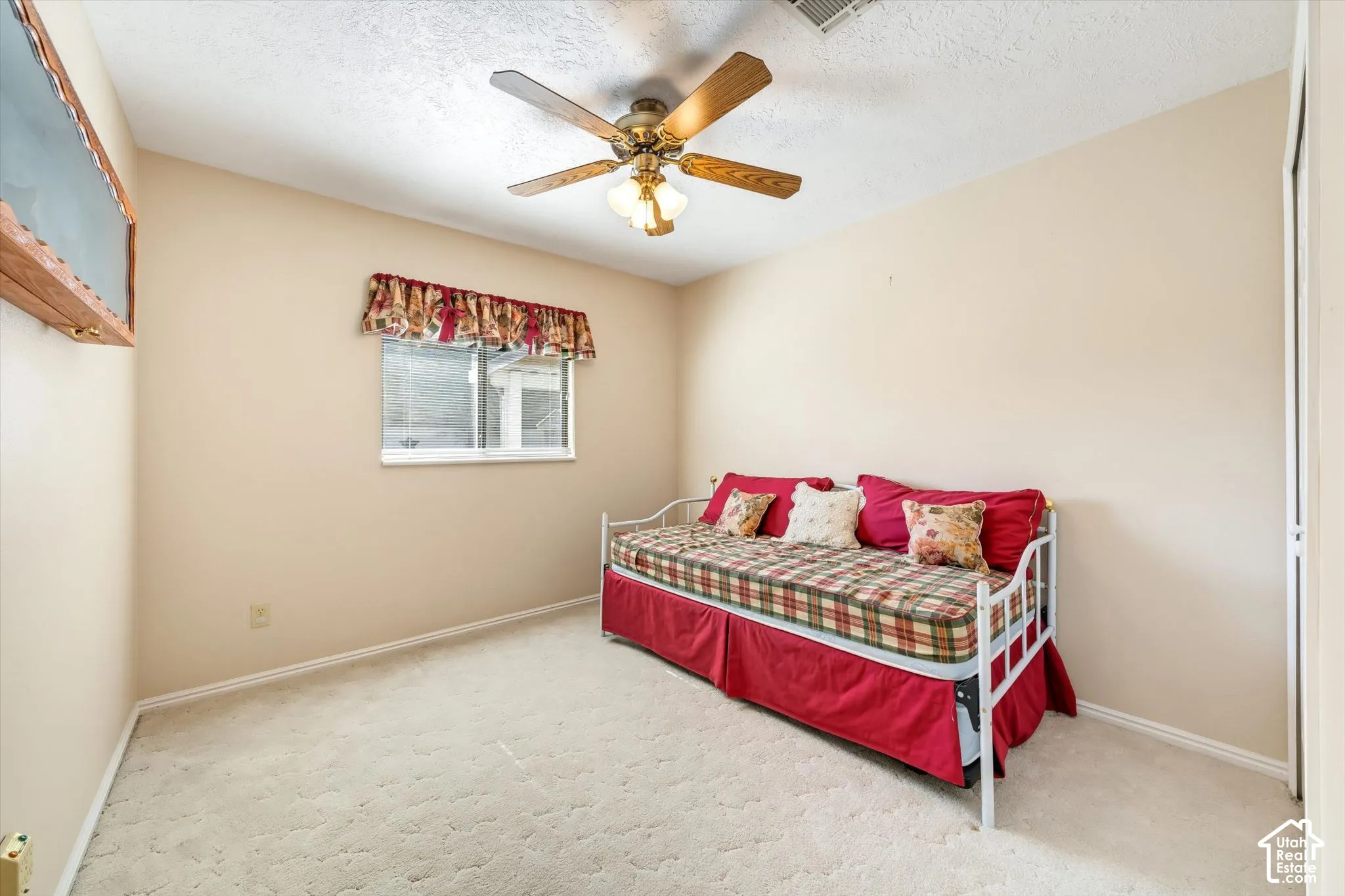 Neutral-toned interior space featuring light-colored wall-to-wall carpeting, a single-pane sliding window, and a ceiling-mounted fan with integrated light fixture