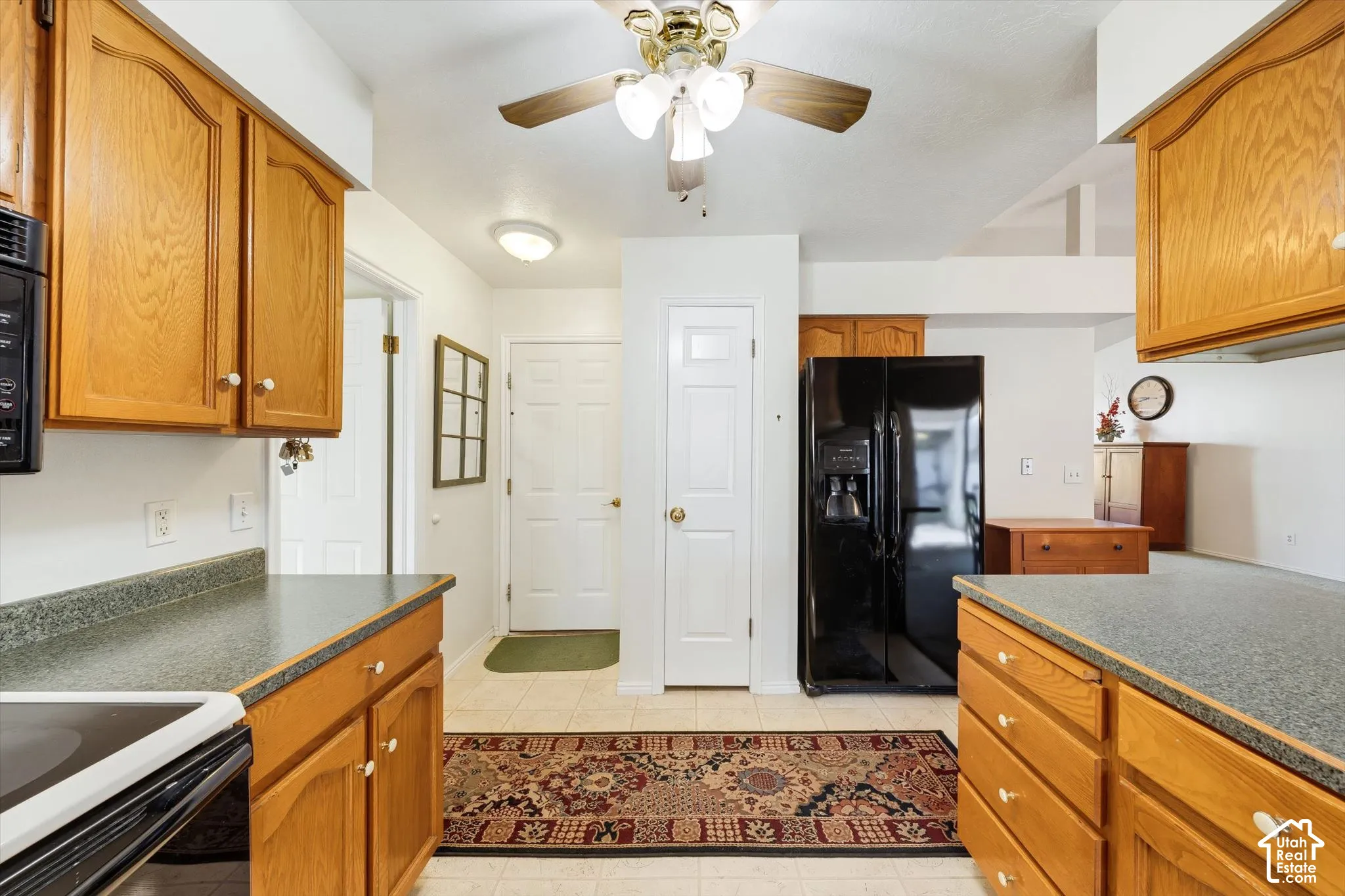 Kitchen featuring natural wood cabinetry, solid surface countertops, a black built-in microwave, a black refrigerator, and a ceiling fan with integrated lighting