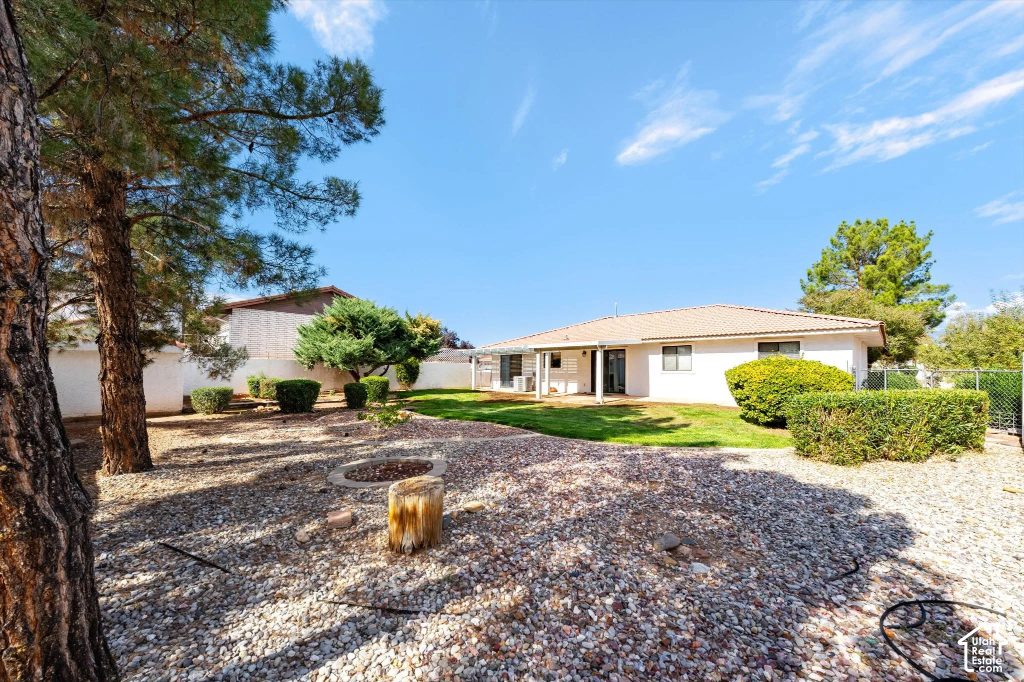 Expansive backyard featuring gravel hardscaping, a manicured lawn, mature trees, ornamental shrubs, and a masonry fire pit