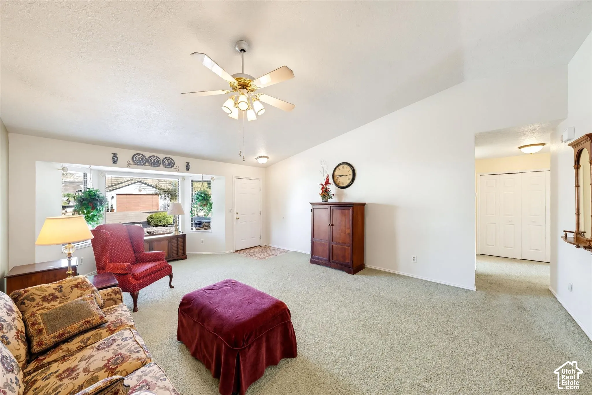 Vaulted ceiling, bay window, carpeted flooring, ceiling fan with multi-bulb light kit, and bi-fold closet doors
