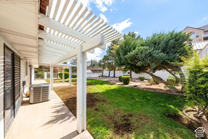 Backyard featuring a white slatted patio cover, concrete patio, grass lawn, mature specimen trees, and perimeter masonry wall