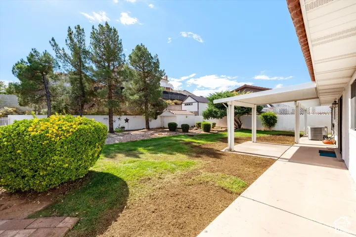Backyard featuring a covered patio, lawn area, perimeter masonry wall, mature trees, and a detached structure