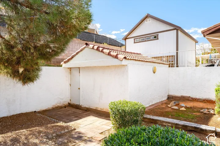 Exterior area featuring a stucco outbuilding with a tile roof, enclosed by a perimeter wall, stone-paved walkways, and established landscape greenery