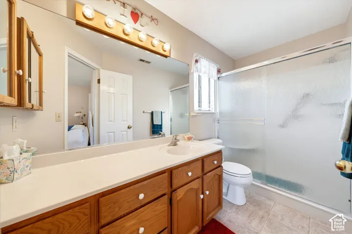 Bathroom featuring a wood vanity with integrated basin, full-width wall mirror, five-bulb vanity light, and a shower enclosure with textured glass doors