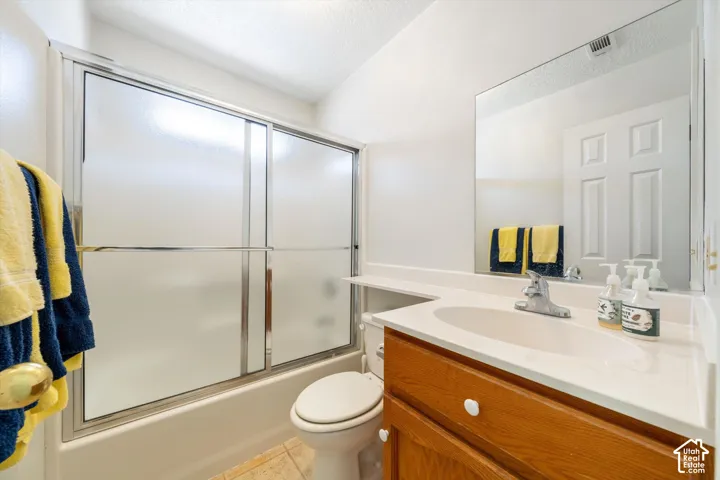 Bathroom featuring a wooden vanity with a seamless integrated countertop and basin, chrome faucet, full-width mirror, and a tub-shower combination with sliding frosted glass doors