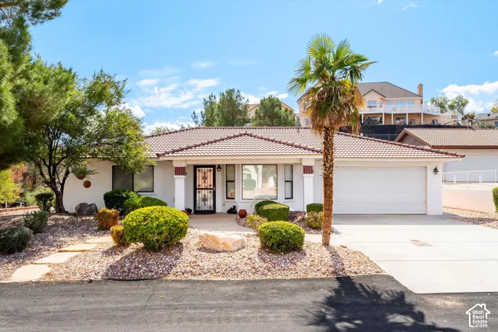 Single-level exterior featuring a tile roof, light-toned stucco siding, decorative column accents, and a concrete driveway leading to an attached two-car garage