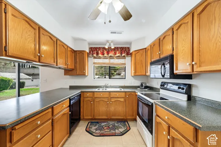 Kitchen featuring oak cabinetry, dark solid-surface countertops, dual-basin stainless steel sink, tile flooring, and integrated black appliances