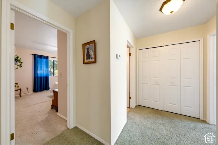Hallway featuring dual-paneled bi-fold closet doors, wall-mounted thermostat, and overhead flush-mount lighting