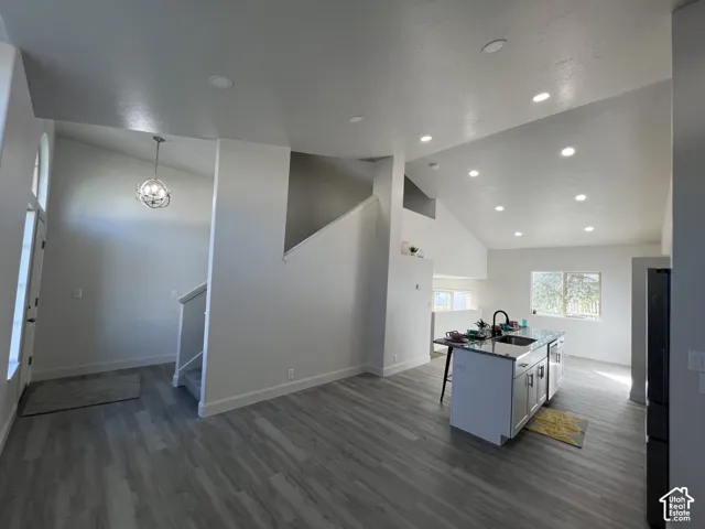 Vaulted ceilings with recessed lighting, wood-finish flooring, kitchen island with stone countertop, and pendant lighting