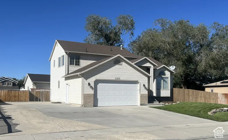 Two-story residence featuring light-toned horizontal siding, a masonry veneer accent, an attached two-car garage, and an expansive concrete driveway