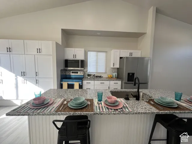 Kitchen featuring a large island with stone-finish countertops, matte black faucet, shaker-style white cabinetry, and vaulted ceilings