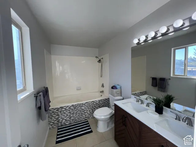 Bathroom featuring a double vanity with a stone countertop, chevron-patterned wood-finish cabinetry, bathtub with decorative tile surround, and a large wall-mounted mirror
