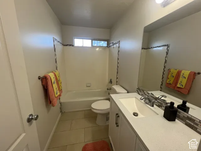 Bathroom featuring a vanity with a white countertop and rectangular undermount sink, ceramic tile flooring, a bathtub-shower combination with tiled accents, and a large wall-mounted mirror