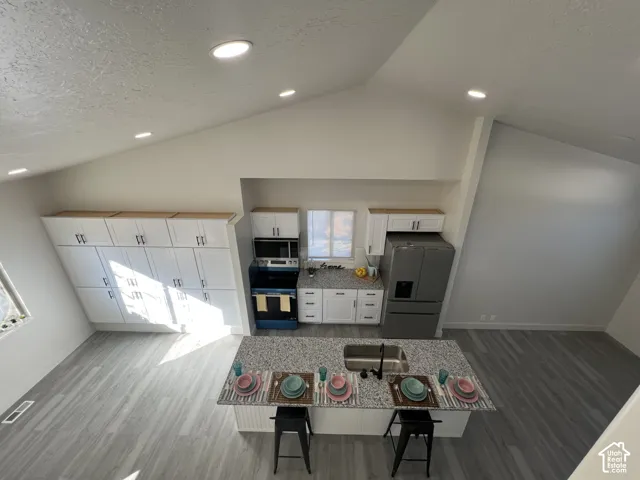 Kitchen featuring vaulted ceilings, recessed lighting, white cabinetry, speckled stone-surface countertops, and wood-finish flooring