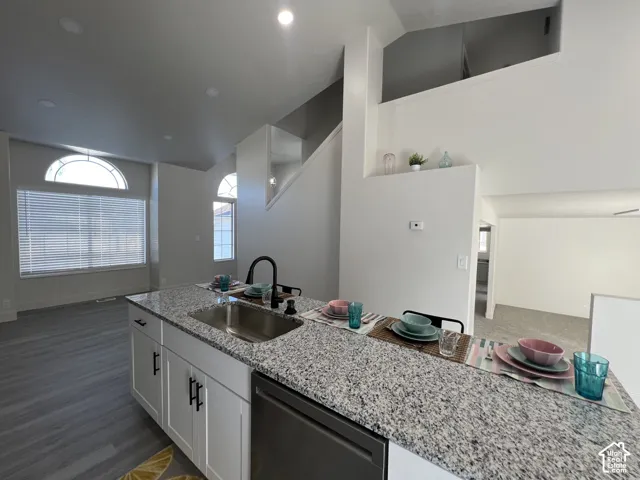 Kitchen featuring a speckled stone-surfaced island, stainless steel undermount sink, matte black faucet, white shaker-style cabinetry, and wood-finish flooring