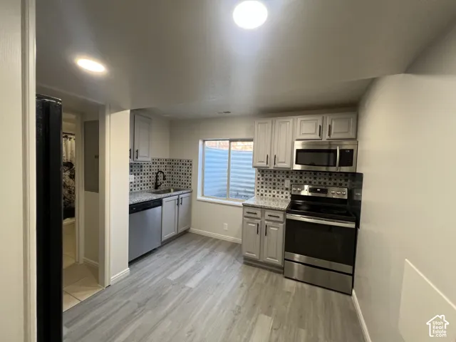 Kitchen featuring light-gray cabinetry, stone-finish countertops, stainless steel appliances, decorative tile backsplash, and wood-finish flooring