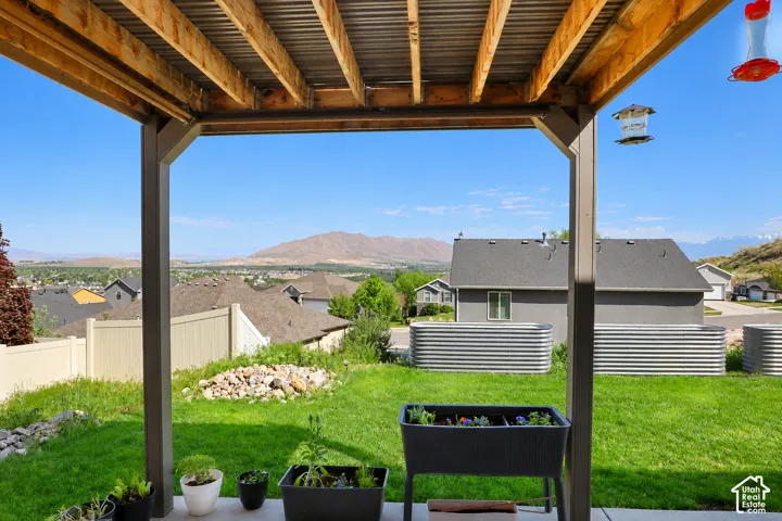Covered patio featuring an exposed-beam wood ceiling, concrete flooring, and metal structural supports, overlooking a backyard with mountain scenery