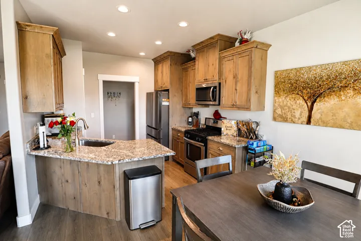 Kitchen featuring wood cabinetry, stone-surface countertops, stainless steel appliances, wood-finish flooring, and recessed ceiling lighting