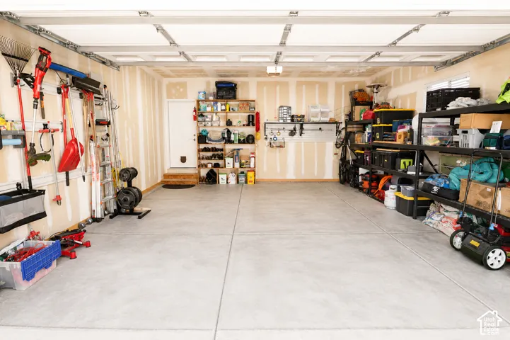 Multi-car garage featuring a concrete floor, built-in track wall storage systems, and a dedicated service door
