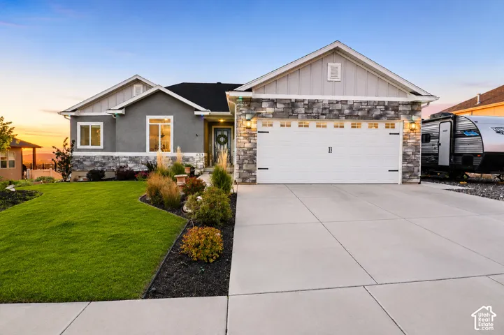 Exterior featuring a stone veneer facade, vertical board-and-batten siding, a wide concrete driveway, an attached two-car garage, and curated landscaping