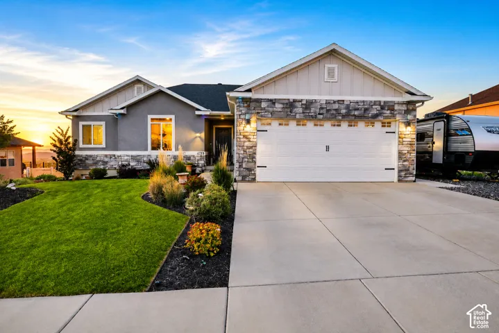 Single-level exterior featuring a stone and siding facade, covered entryway, attached multi-car garage, and concrete driveway