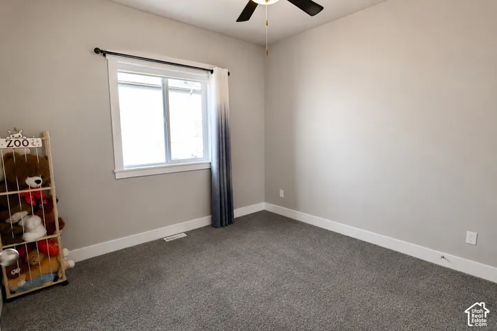 Neutral-toned interior featuring wall-to-wall carpeting, window with trim casing, and a ceiling fan