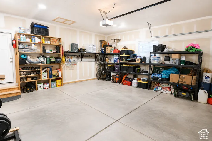 Spacious two-car garage featuring finished drywall, a concrete floor, an automated overhead door opener, and a dedicated exterior access door