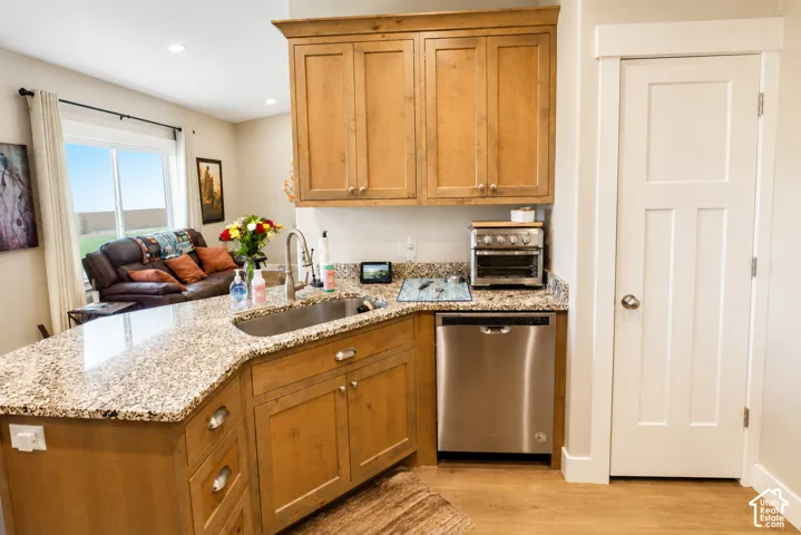 Kitchen featuring wood cabinetry, stone countertops, stainless steel undermount sink, built-in stainless steel dishwasher, and solid-core interior door