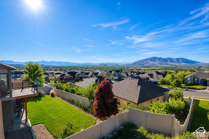 Elevated backyard featuring a grass lawn, privacy fencing, and a wooden balcony with black metal railings, complemented by a prominent mountain range backdrop