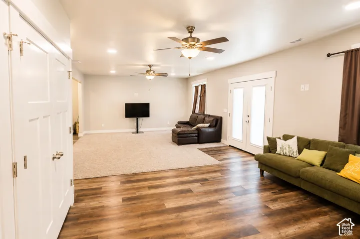 Spacious room featuring wood-finish flooring, neutral carpeting, recessed lighting, dual ceiling fans, and French doors