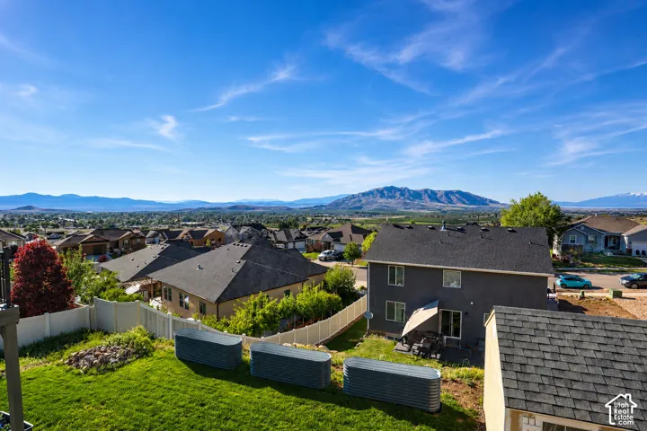 Elevated rear yard featuring a lawn, mature landscaping, and corrugated metal planter boxes, enclosed by a white vinyl privacy fence with mountain range backdrop