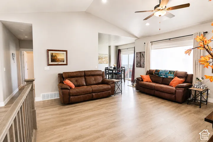 Vaulted ceilings featuring a central paddle fan, wood-finish flooring, and a sliding glass door