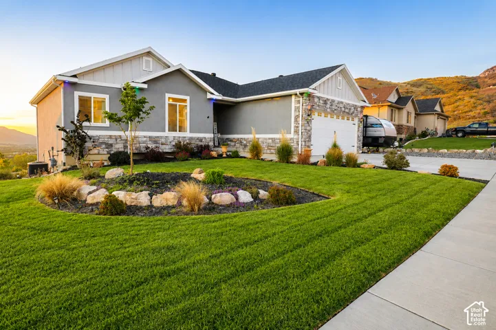 Single-story exterior featuring a stone and stucco facade, an attached two-car garage, and manicured landscaping with natural stone accents