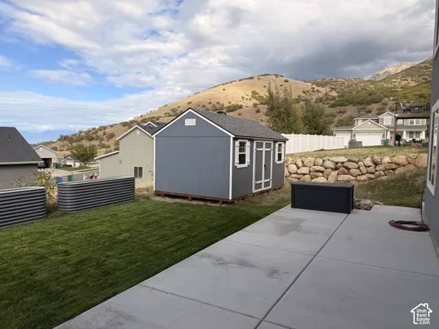 Rear yard featuring a concrete patio, lawn area, two corrugated metal raised garden beds, and a detached storage shed set against a mountainous backdrop
