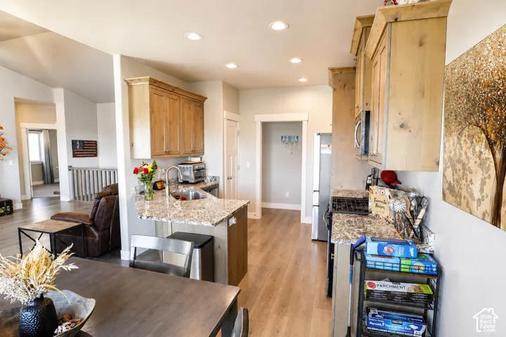 Kitchen featuring natural wood-finish cabinetry, patterned stone-finish countertops, stainless steel undermount sink, recessed lighting, and wood-finish flooring