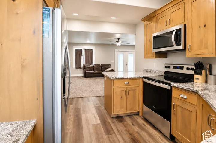 Kitchen featuring custom wood cabinetry, stone-patterned countertops, stainless steel appliances, and wood-finish flooring
