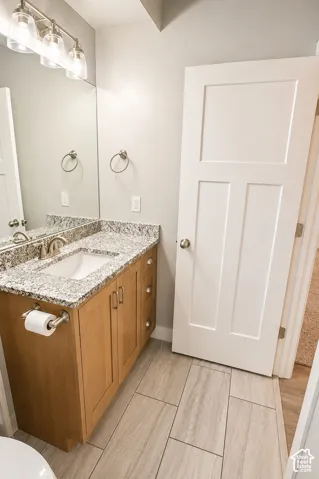 Bathroom featuring a natural wood-finish vanity, stone-patterned countertop with an undermount sink, multi-light fixture, and tile flooring