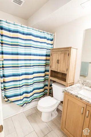 Bathroom featuring light-toned wood-finish cabinetry, speckled countertop with an integrated basin, and large-format rectangular floor tile