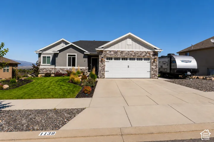 Single-story exterior featuring a stone and stucco facade, a multi-gabled roofline, a two-car garage, and a concrete driveway