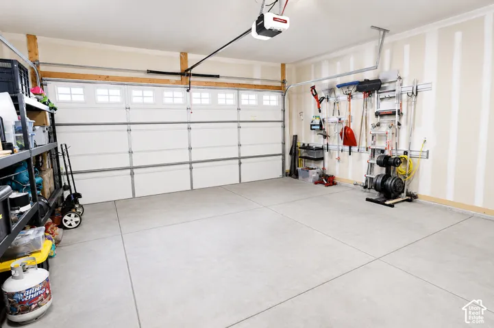 Attached multi-vehicle garage featuring a sectional door with windows, smooth concrete flooring, and wall-mounted storage track systems