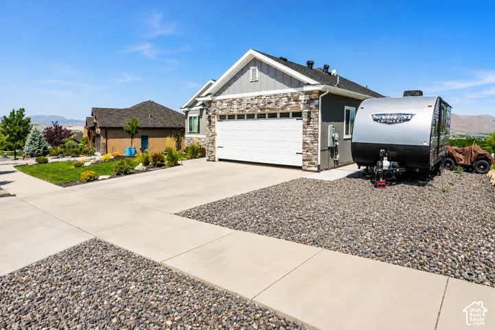 Exterior featuring stone veneer accents, vertical siding, concrete driveway, attached two-car garage, and gravel side yard area
