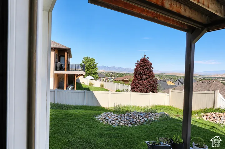 Covered patio featuring a timber-frame support beam, vinyl privacy fencing, landscaped rock features, and mountain scenery