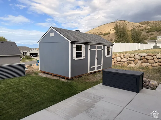 Detached storage structure featuring painted siding, white trim, dual-pane windows with shutters, and asphalt shingle roofing, set against a backdrop of mountainous terrain