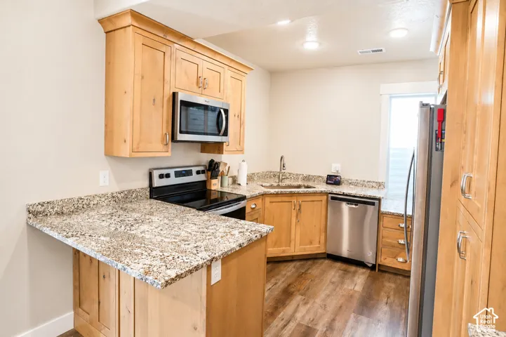 Kitchen featuring light-finish cabinetry, stone-surface countertops, wood-finish flooring, and stainless steel appliances including a built-in microwave and dishwasher