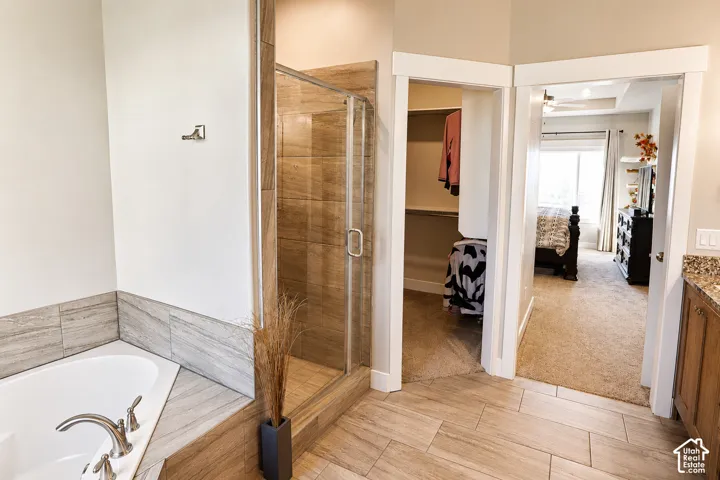 Bathroom featuring a drop-in soaking tub, walk-in shower with tile surround, wood-finish floor tiling, and wood cabinetry